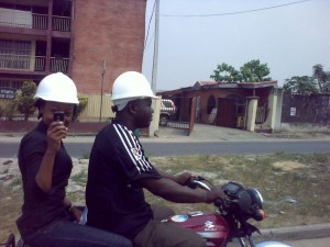 An okada operator and his passenger in Lagos Nigeria. Note that they are both wearing helmets meant for construction workers