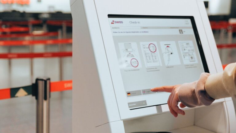 A passenger touches the screen of a self-service check-in kiosk at an airport