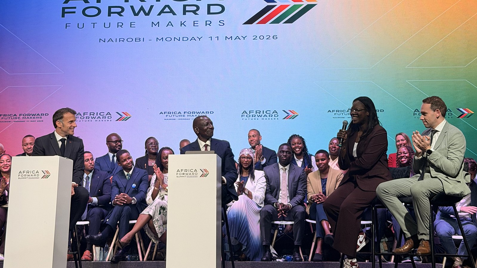 Press photo from the Africa Forward Summit in Nairobi on 11 May 2026 showing French President Emmanuel Macron at the left lectern, Kenyan President William Ruto at the centre lectern, and Amini chief executive Kate Kallot with Foxconn AI head Jesse Chao on the right of the stage