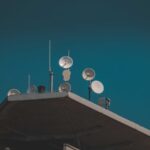 Low-angle view of communication dishes and antennas mounted on a building against the sky