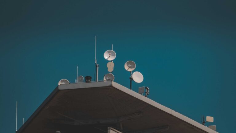 Low-angle view of communication dishes and antennas mounted on a building against the sky