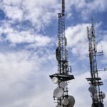 Telecommunications tower carrying antennas and satellite dishes against a bright sky