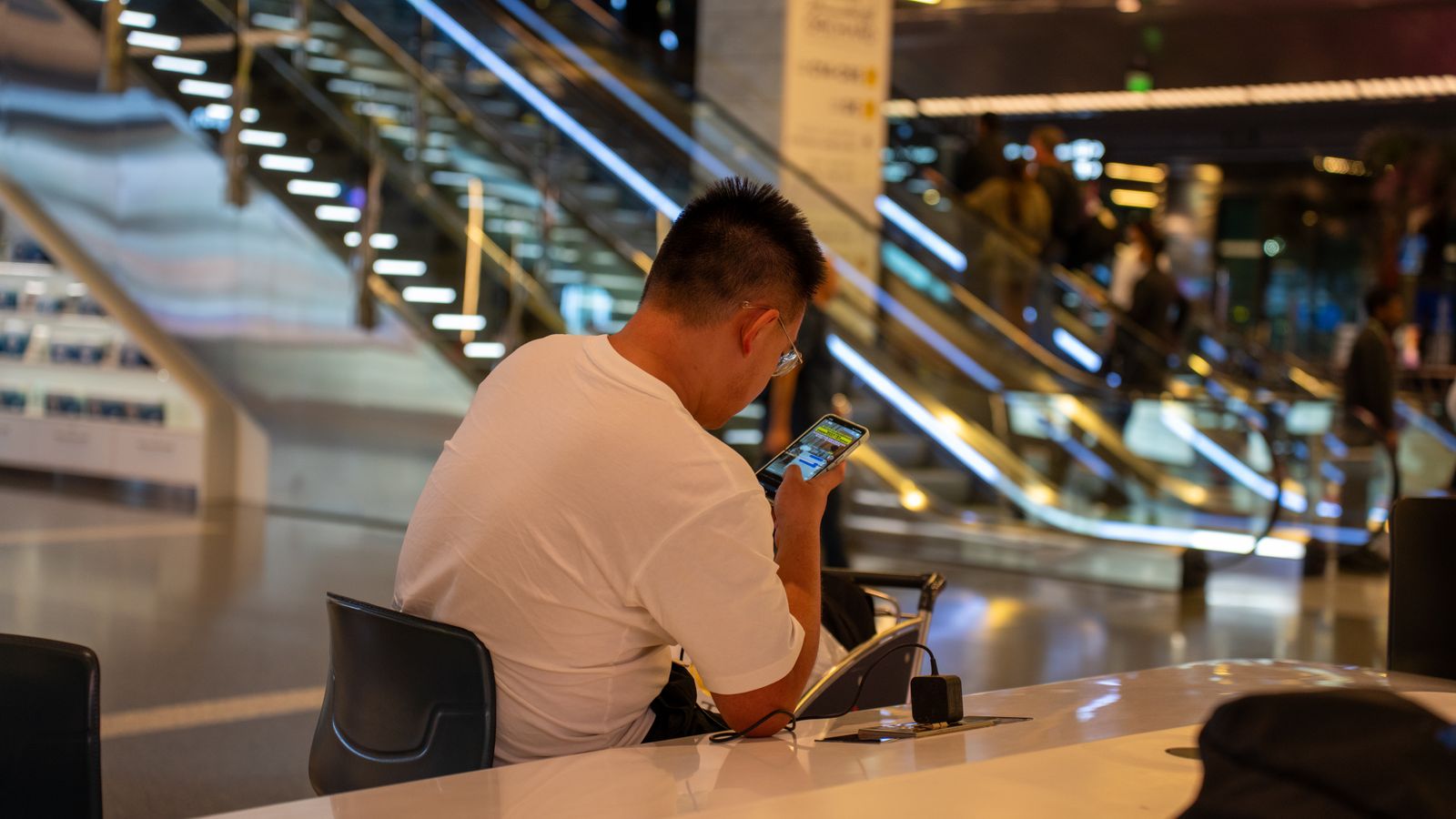 A traveller uses a smartphone while seated in a modern airport terminal.