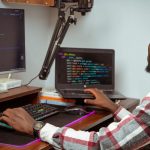 An African developer coding at a desktop and laptop