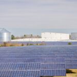 A large solar panel field beside industrial buildings