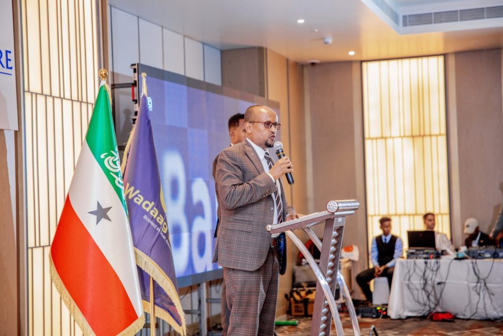 Q&A: building a digital Islamic bank in Somaliland 7 A speaker addresses the Wadaag Bank launch ceremony from a podium beside the Somaliland national flag and a Wadaag Bank flag.
