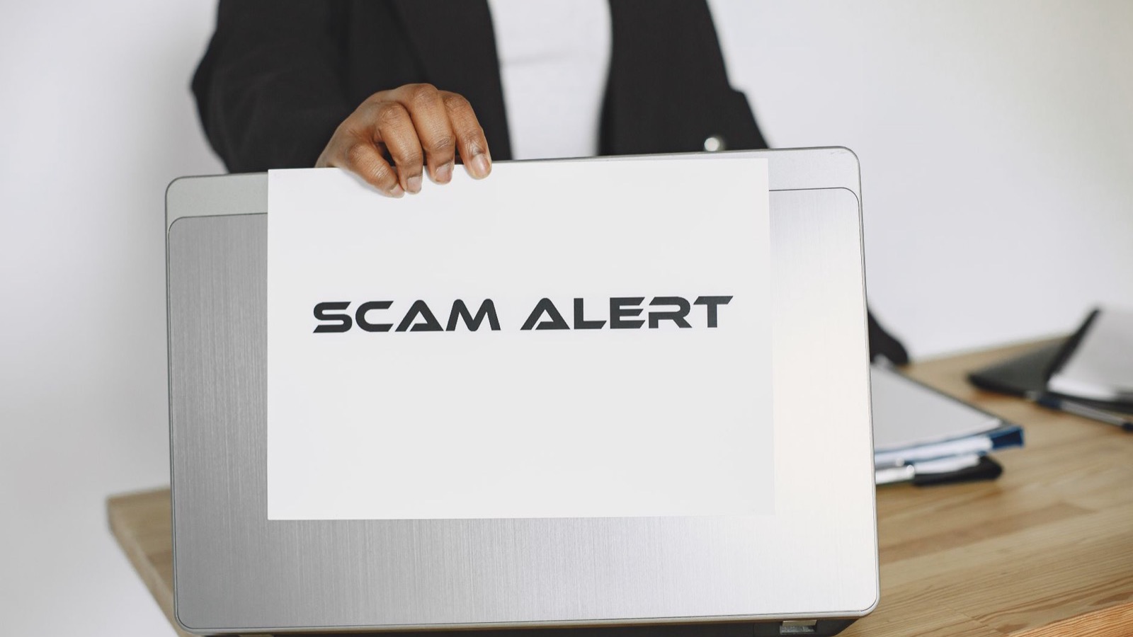 Hand holding a scam alert warning sign next to a laptop